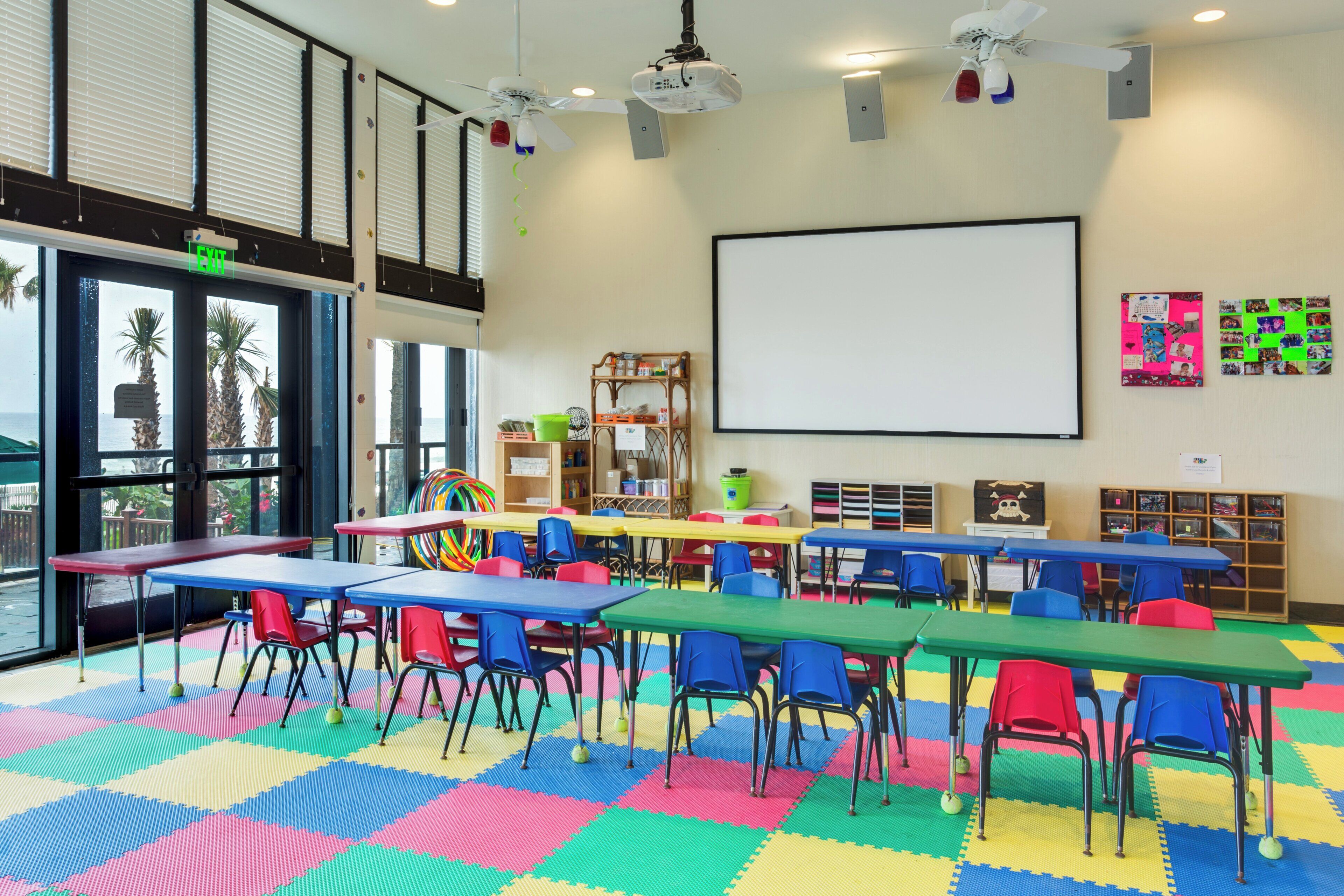 A classroom with colorful tables and chairs, a whiteboard, and educational materials on shelves.