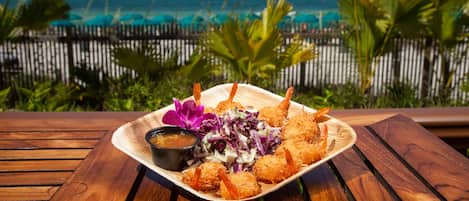 A wooden table with a plate of fried shrimp and salad, set against a view of the ocean and beach.