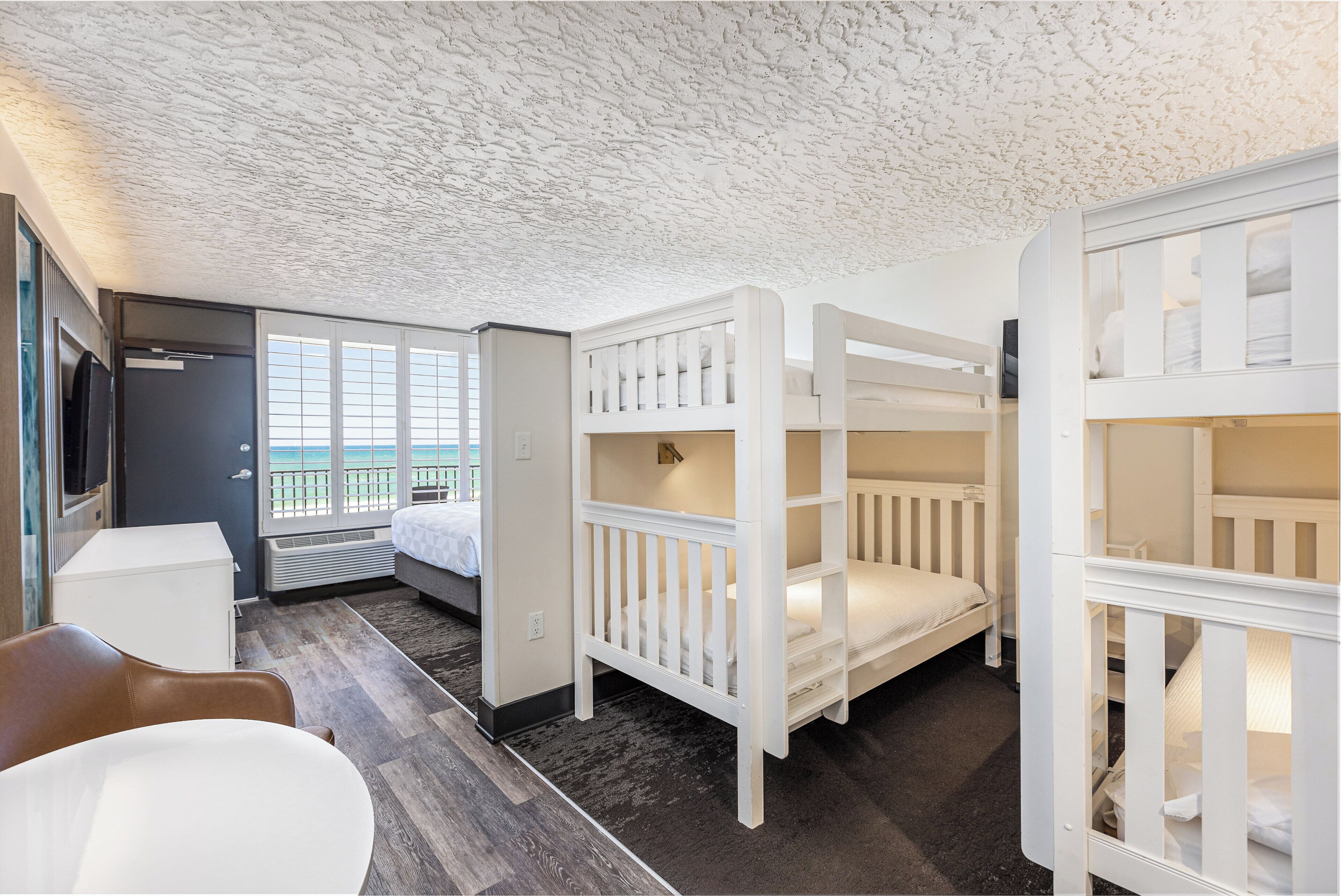 A room with bunk beds, a desk, a chair, and a view of the sea.