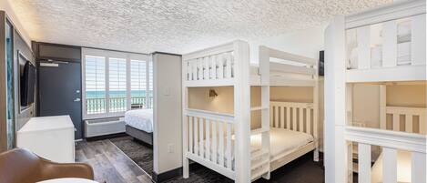 A room with bunk beds, a desk, a chair, and a view of the sea.
