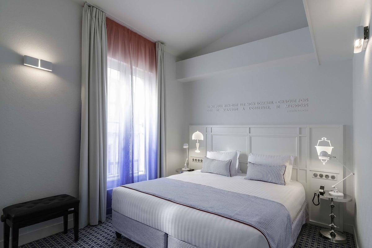 Une chambre d’hôtel avec un grand lit, des lampes de chevet, un banc et un mur agrémenté d’un luminaire décoratif.