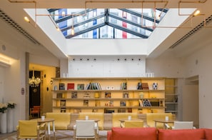 A modern library with bookshelves, seating areas, and a skylight. - Hôtel 34B - Astotel (Paris)