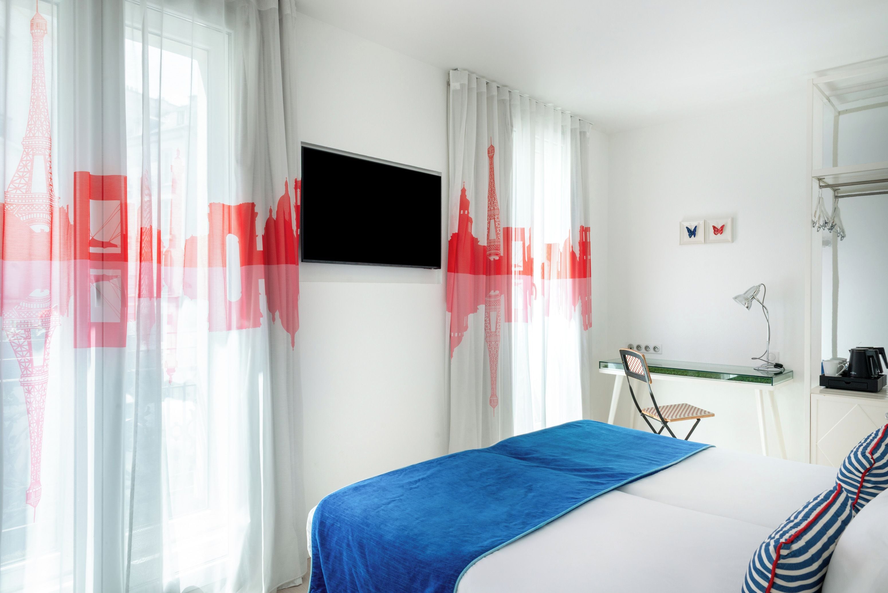 A hotel room with a bed, a desk with a chair, a flat-screen TV, and a window with curtains.