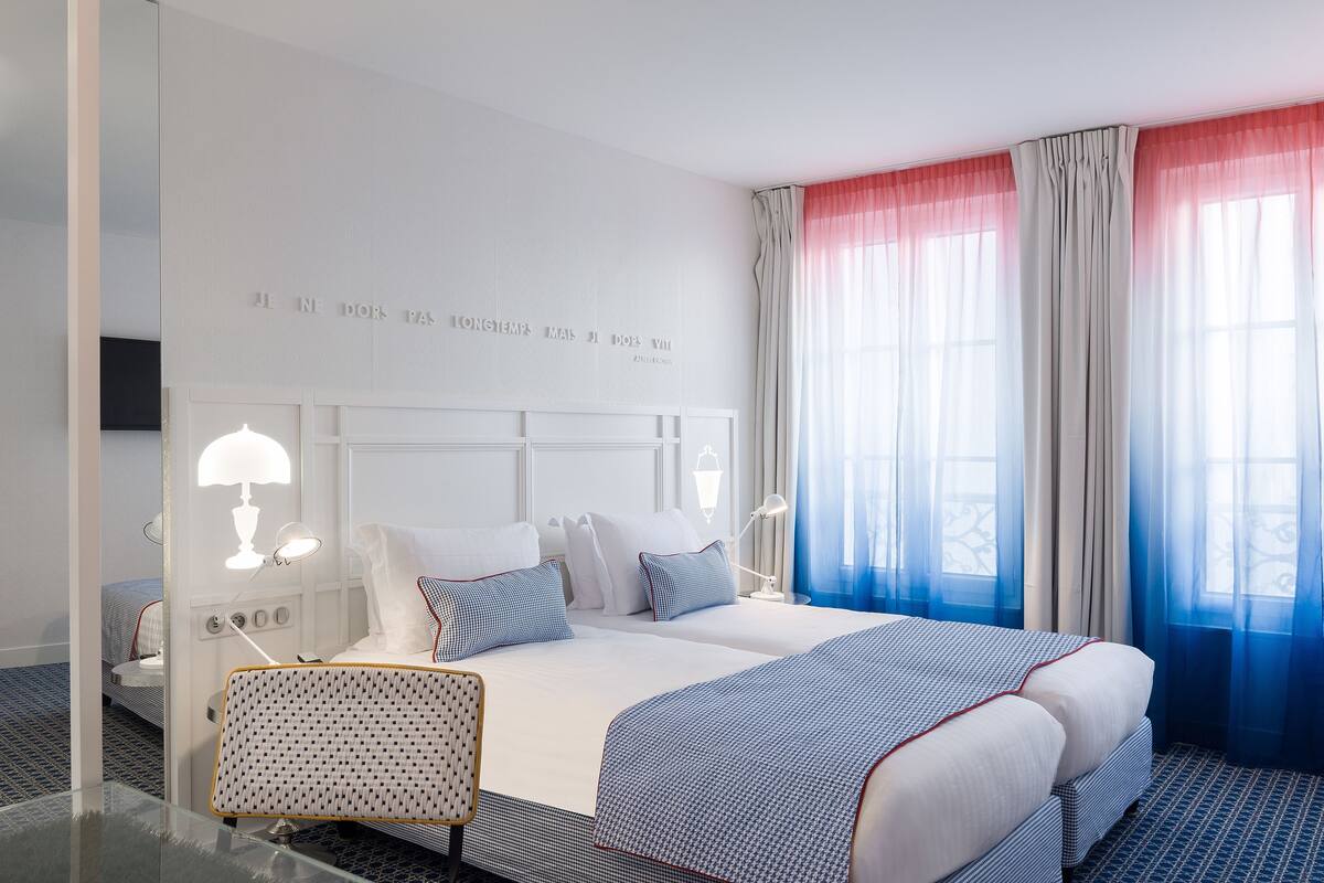 Une chambre d’hôtel avec un grand lit, deux tables de chevet, un miroir et un mur orné d’une inscription décorative.