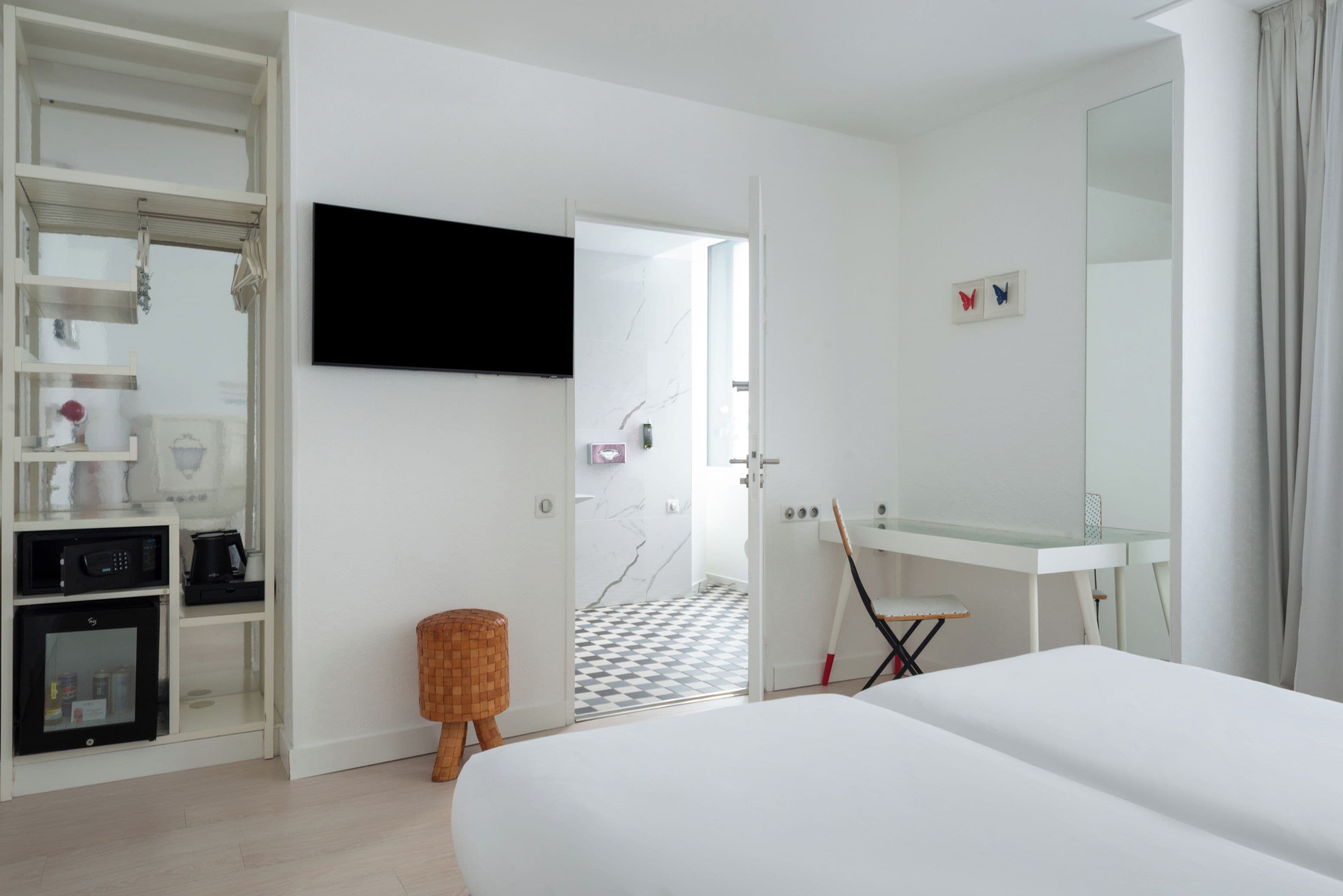 A hotel room with a bed, a TV, a wardrobe, a bathroom with a mirror, and a checkered floor.