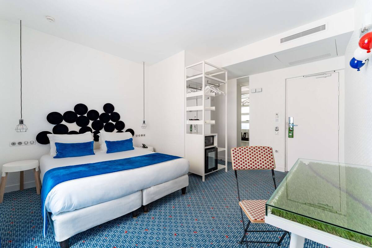 Une chambre d’hôtel moderne dotée d’un grand lit, d’une armoire intégrée, d’une petite table et d’une table avec un plateau en verre et un intérieur vert.