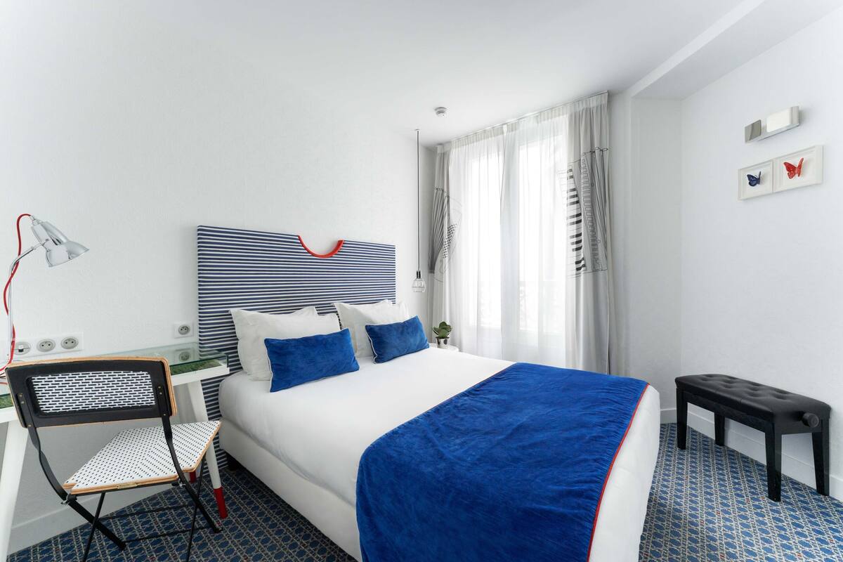 Une chambre d’hôtel avec un grand lit, un bureau avec une chaise, une petite table et une lampe.