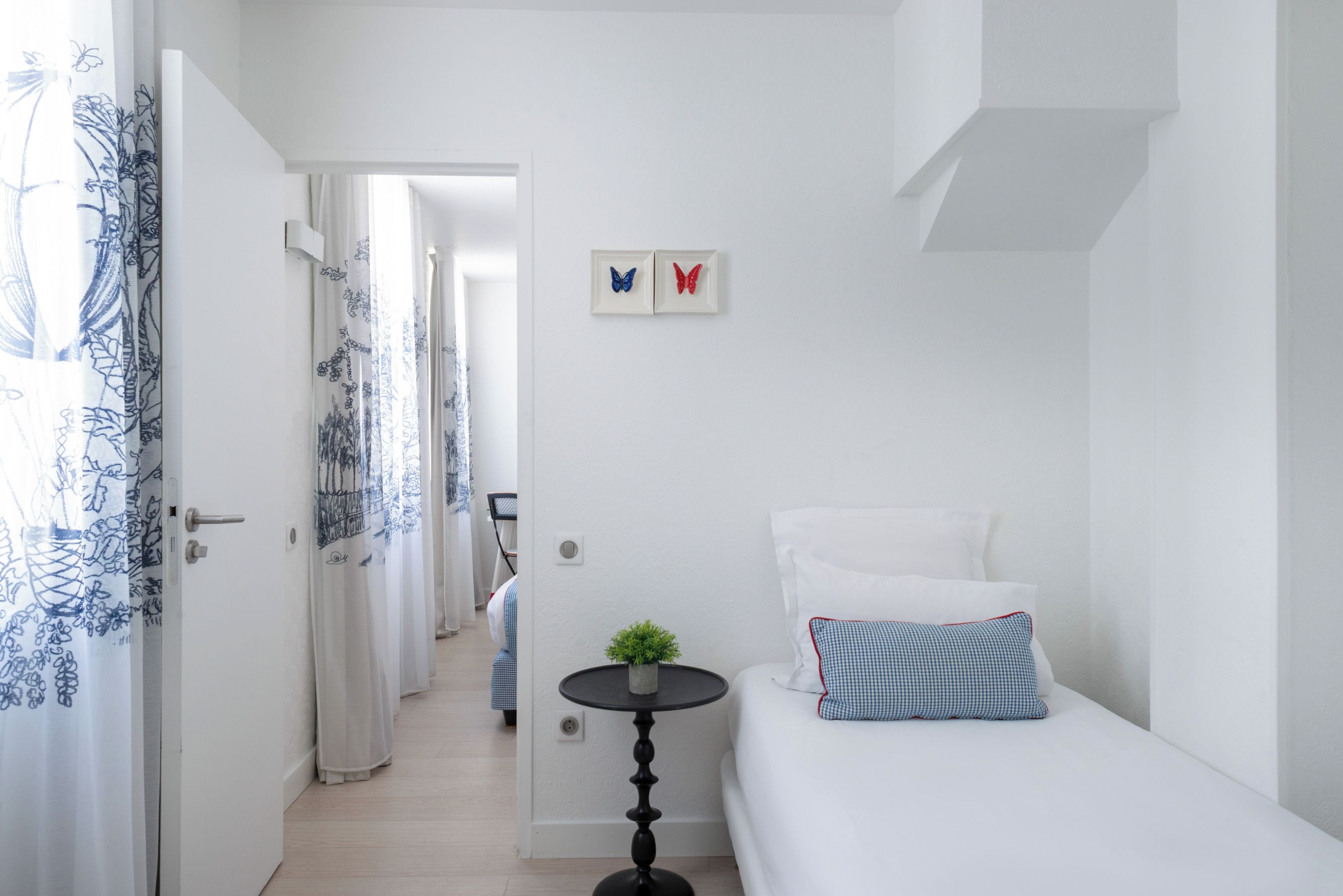 A hotel room with a bed, a small table with a plant, and a view of a hallway.