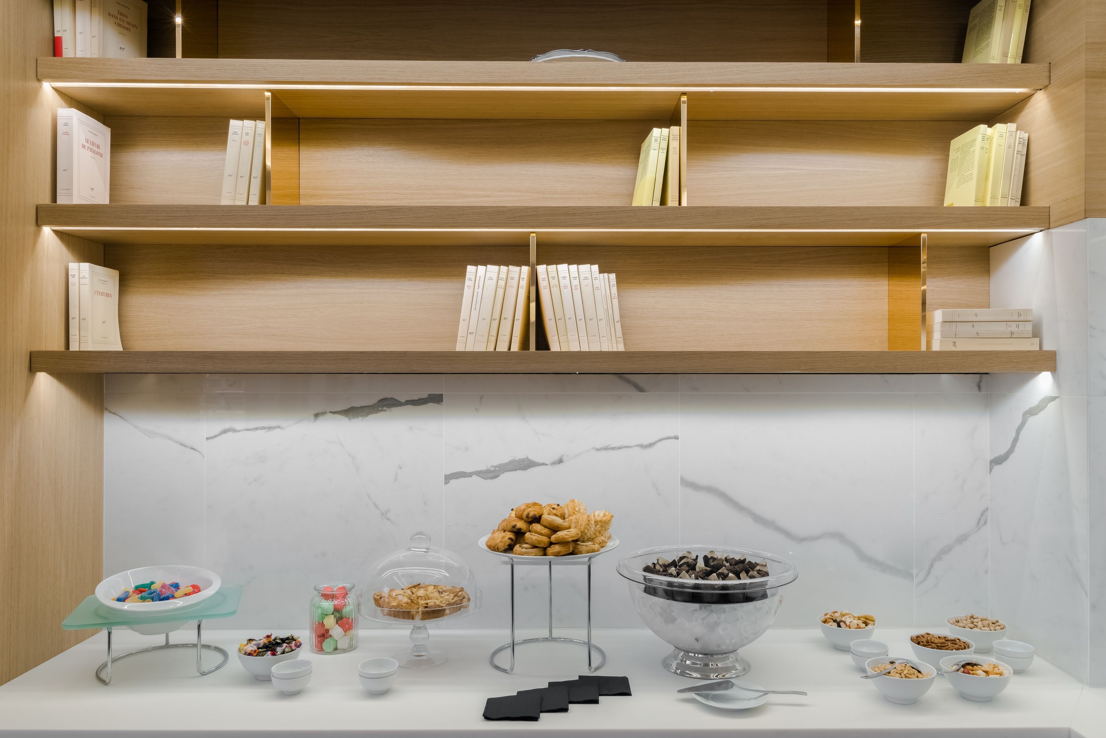 Une cuisine moderne avec des étagères en bois, un dosseret en marbre et divers produits alimentaires exposés sur le plan de travail.