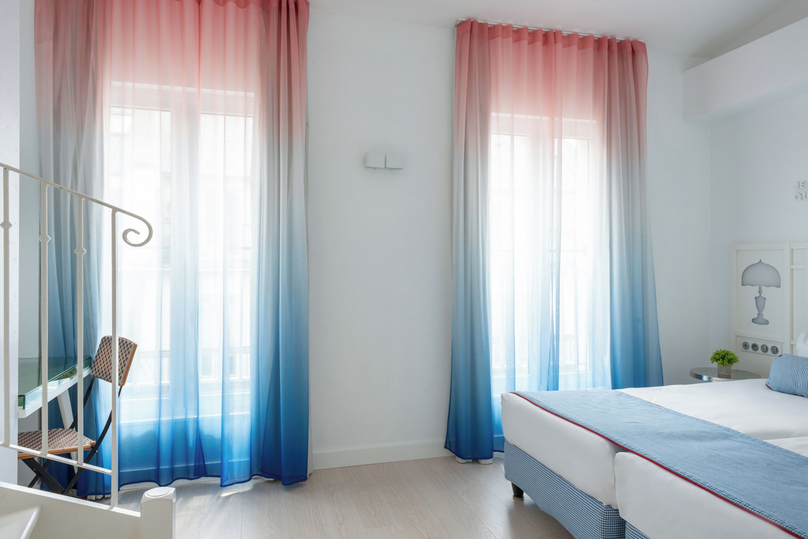 A bedroom with a bed, a chair, a small table with a plant, and curtains.