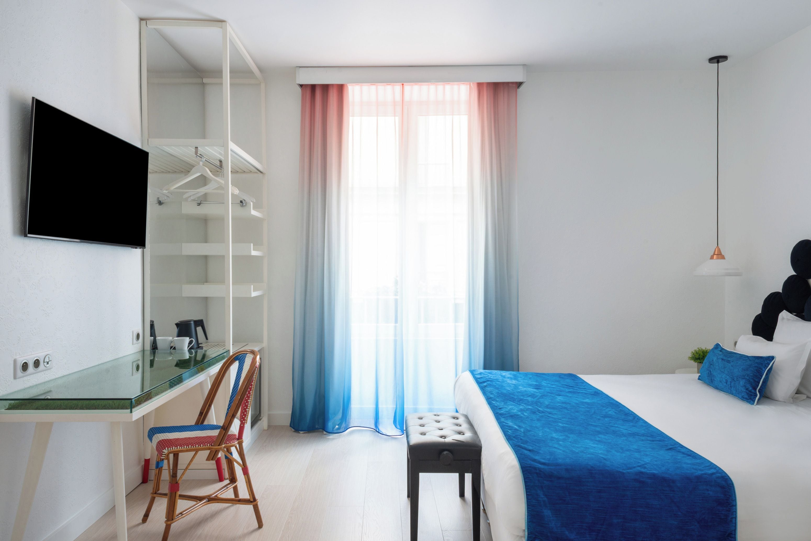 A hotel room with a bed, a desk with a chair, a television, and a window with curtains.