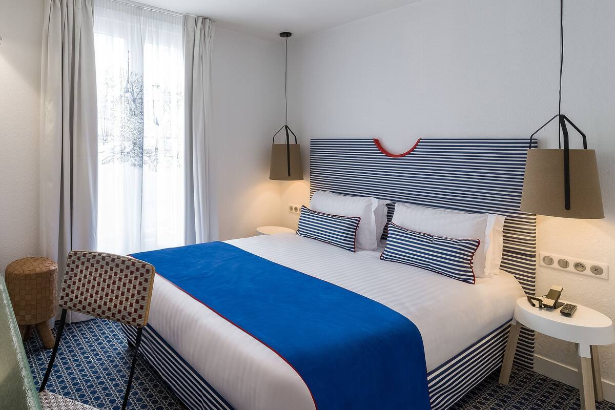 Une chambre d’hôtel avec un lit, une chaise, une table de chevet et une fenêtre avec des rideaux.