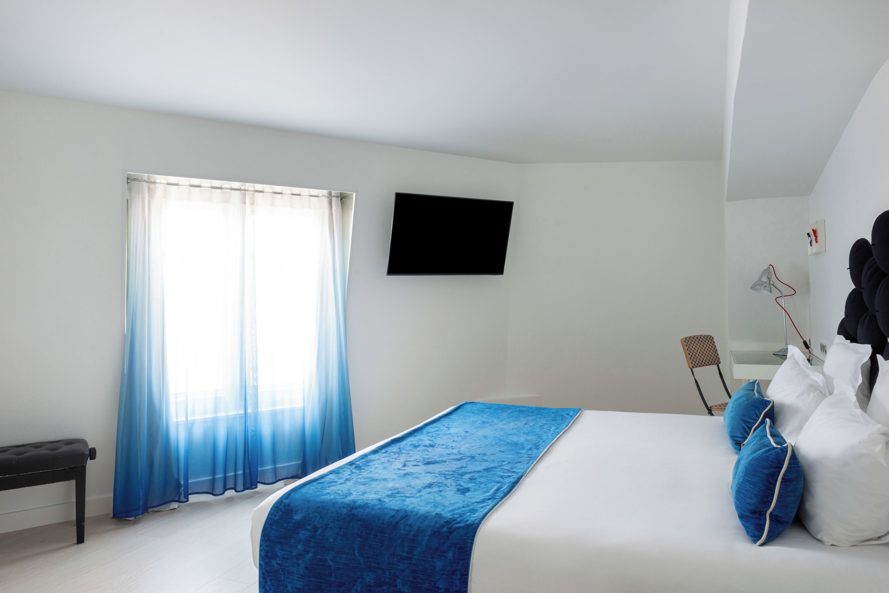 Ein Schlafzimmer mit einem Bett, einem an der Wand montierten Fernseher, einem Sessel und einem Schreibtisch.