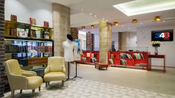 Un hall d’entrée avec un mannequin, deux fauteuils, une bibliothèque rouge et un téléviseur diffusant une image de l’hôtel « 34B ».