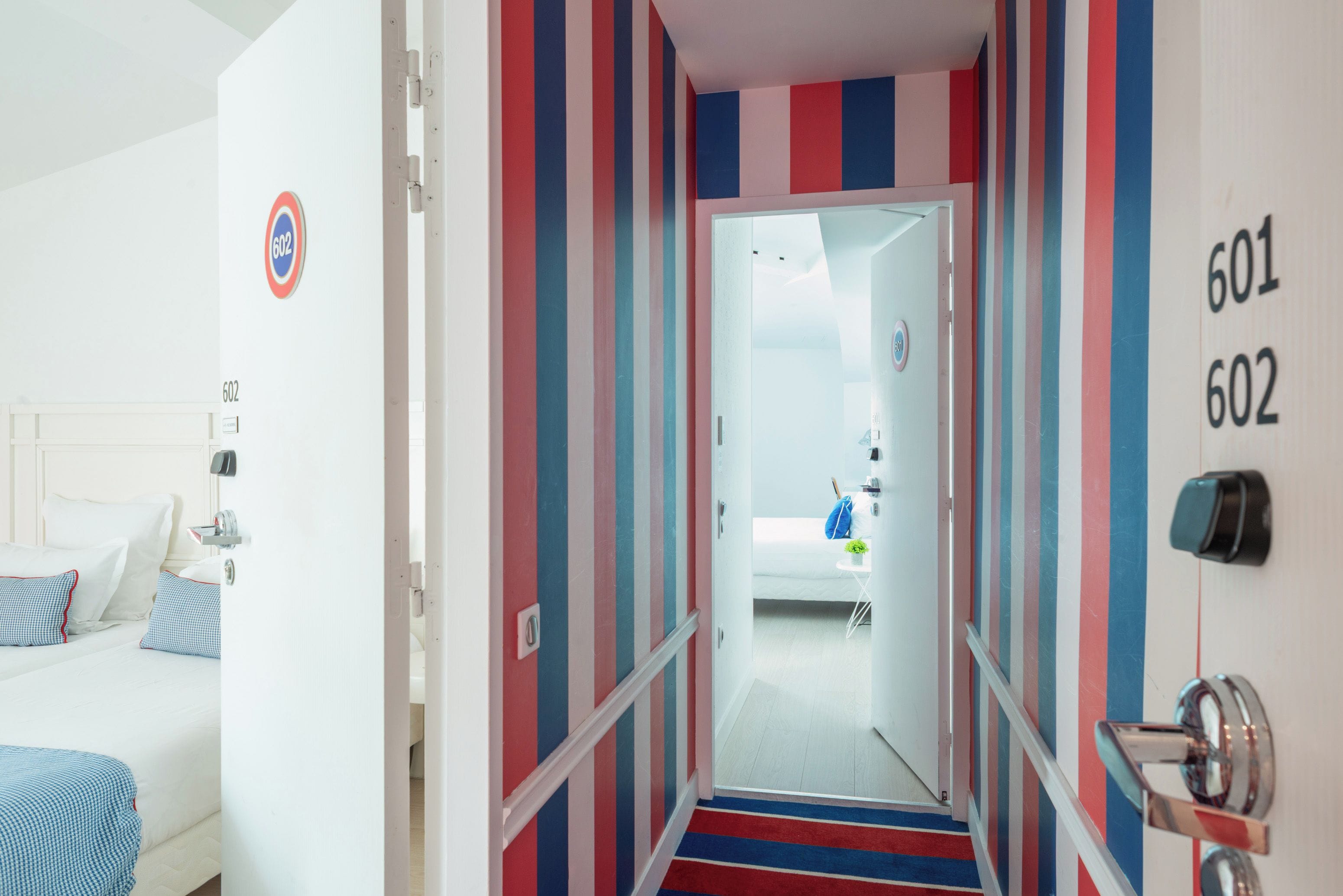 A hotel hallway with striped walls, a bed with checkered bedding, and a staircase leading to another room.