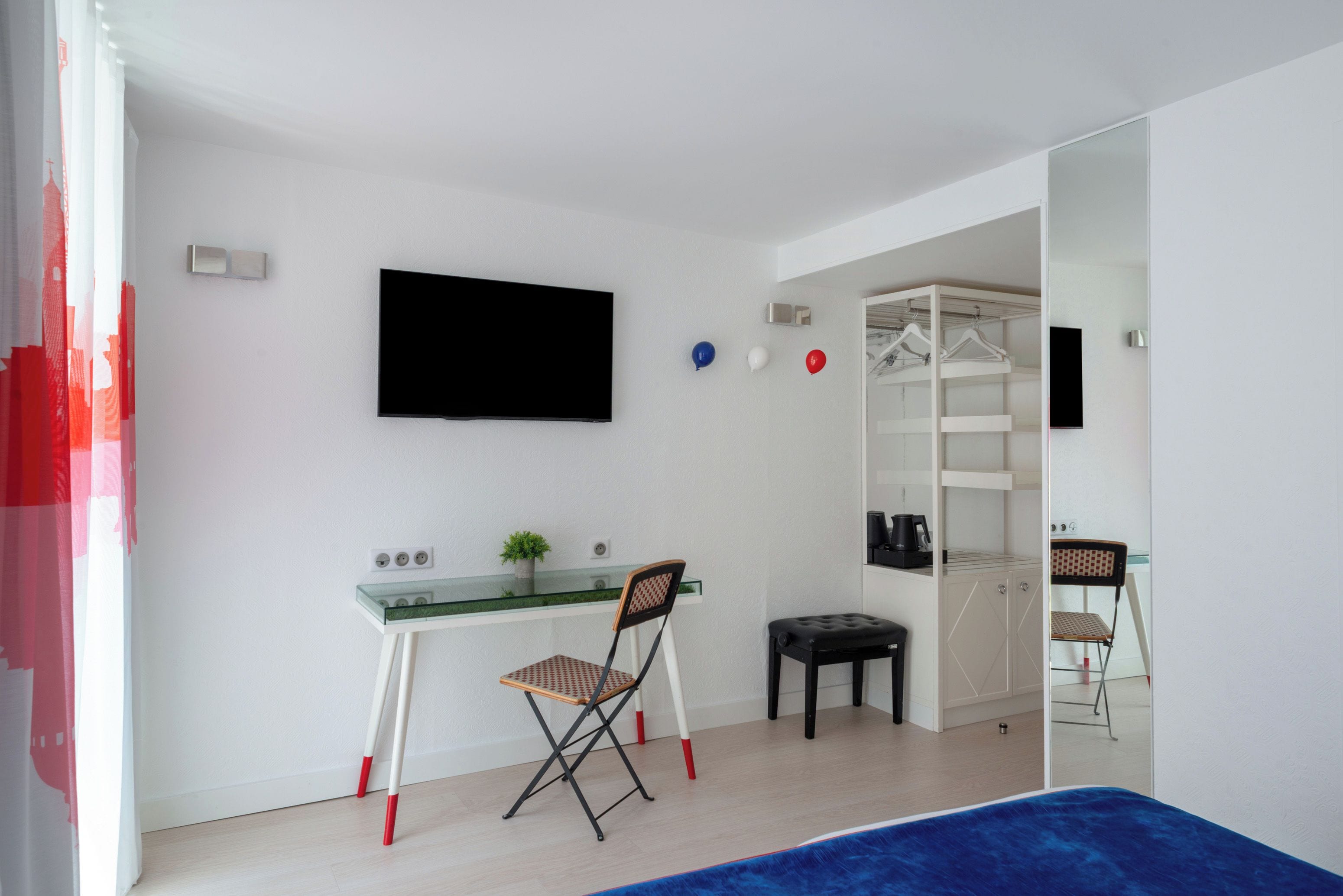 Una habitación moderna con un escritorio de vidrio, una silla, un taburete pequeño, un televisor y un armario con espejo.