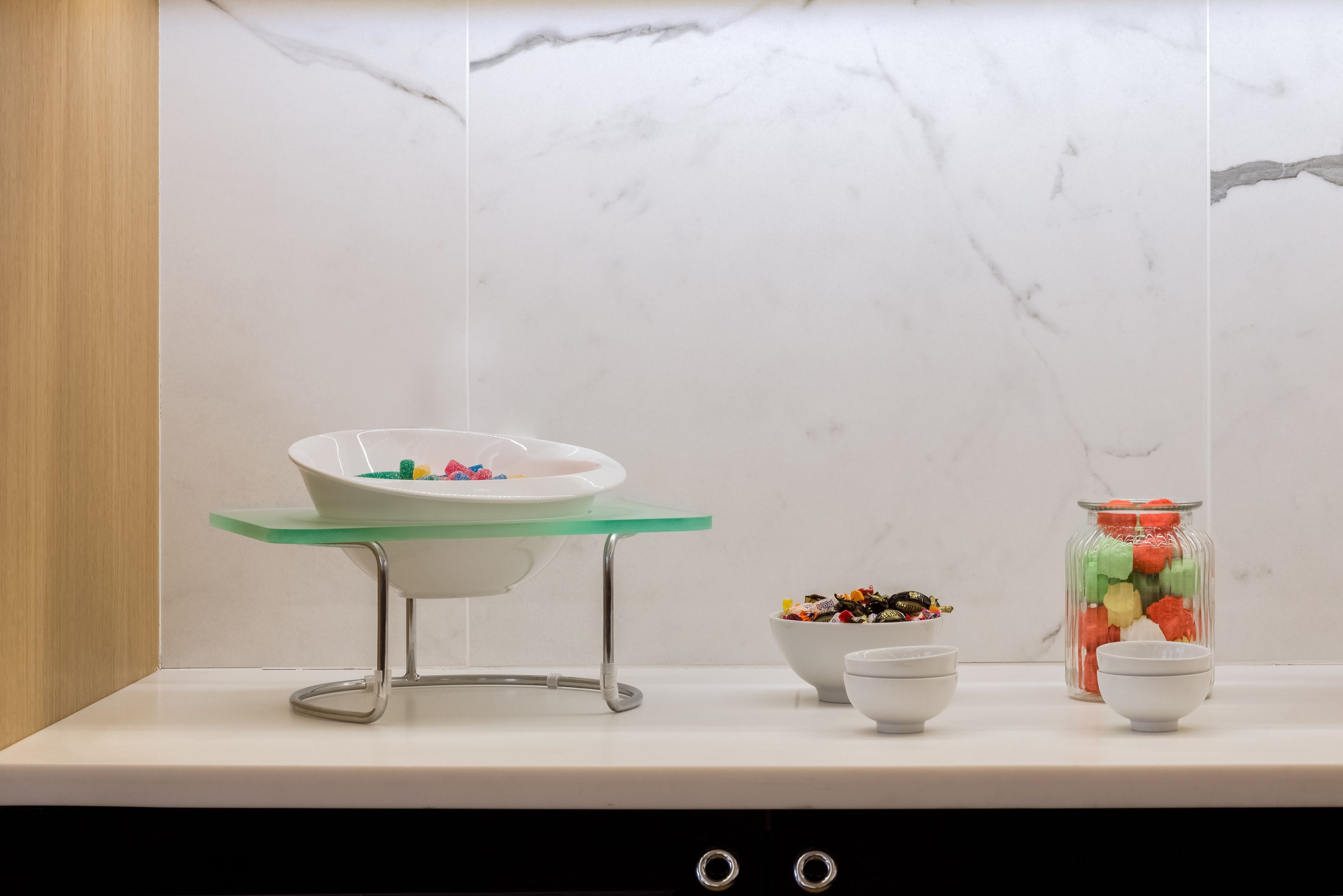 A kitchen counter with a marble backsplash, a glass bowl on a stand, and two bowls with snacks.