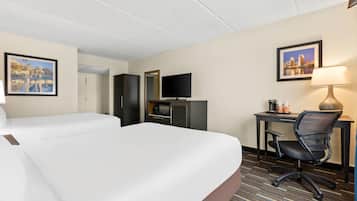 Une chambre d’hôtel avec deux lits, un bureau avec une chaise, une télévision et des tableaux encadrés aux murs.