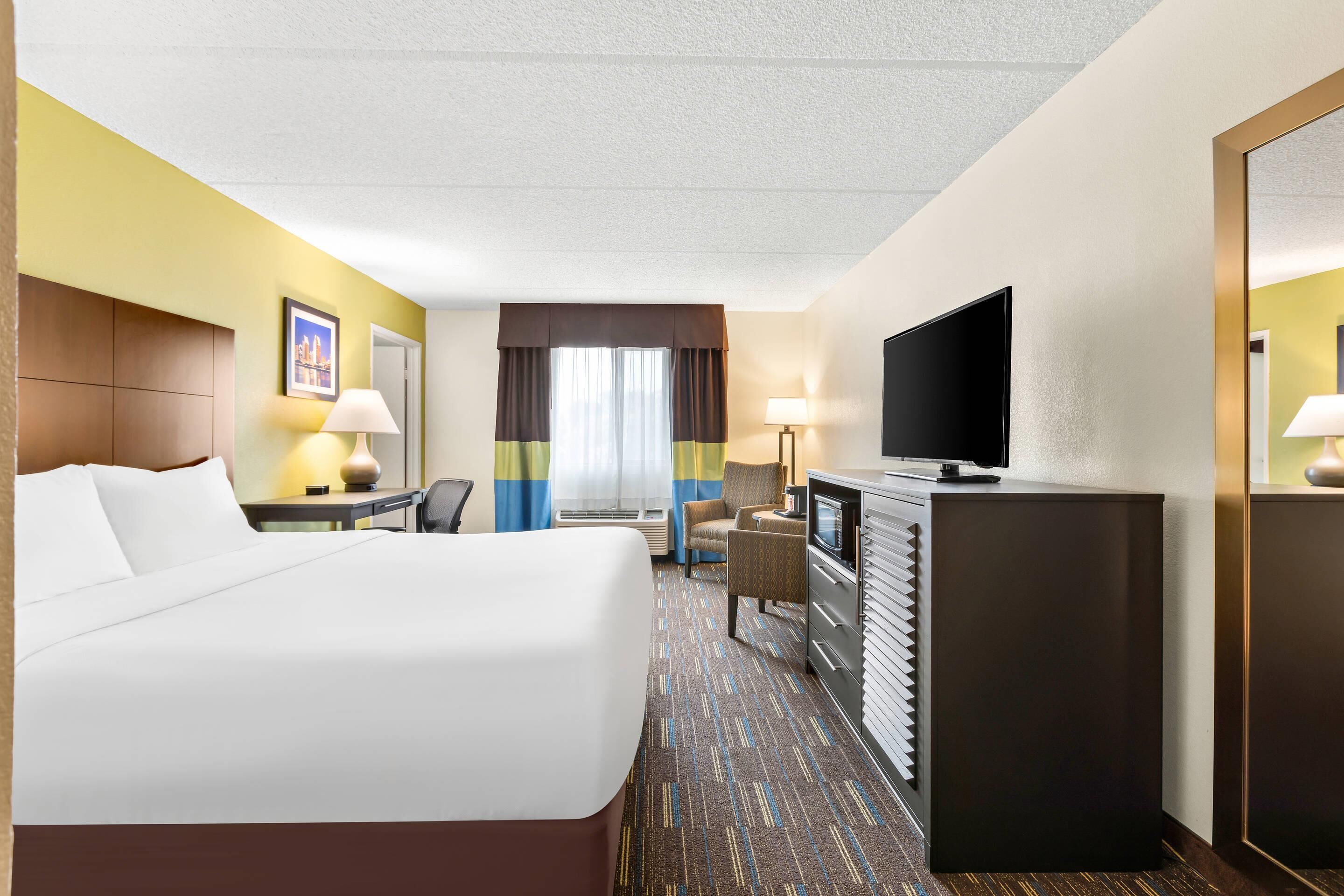 A hotel room with a bed, desk, chair, TV, and a dresser.