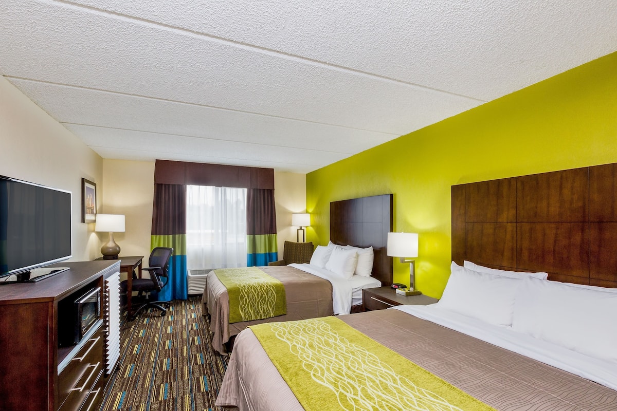 A hotel room with two beds, a desk with a TV, and a window with curtains.
