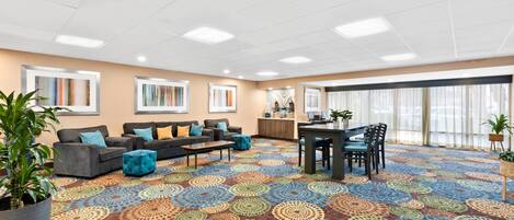 A spacious room with a patterned carpet, a dining area, sofas, and a large window.