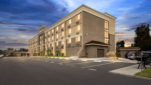 A multi-story hotel with a parking lot, a landscaped area with palm trees, and a clear sky. - Comfort Inn Chula Vista San Diego South (Chula Vista)
