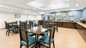 A hotel dining area with tables and chairs, a kitchen counter, and a wall with artwork. - Comfort Inn Chula Vista San Diego South (Chula Vista)