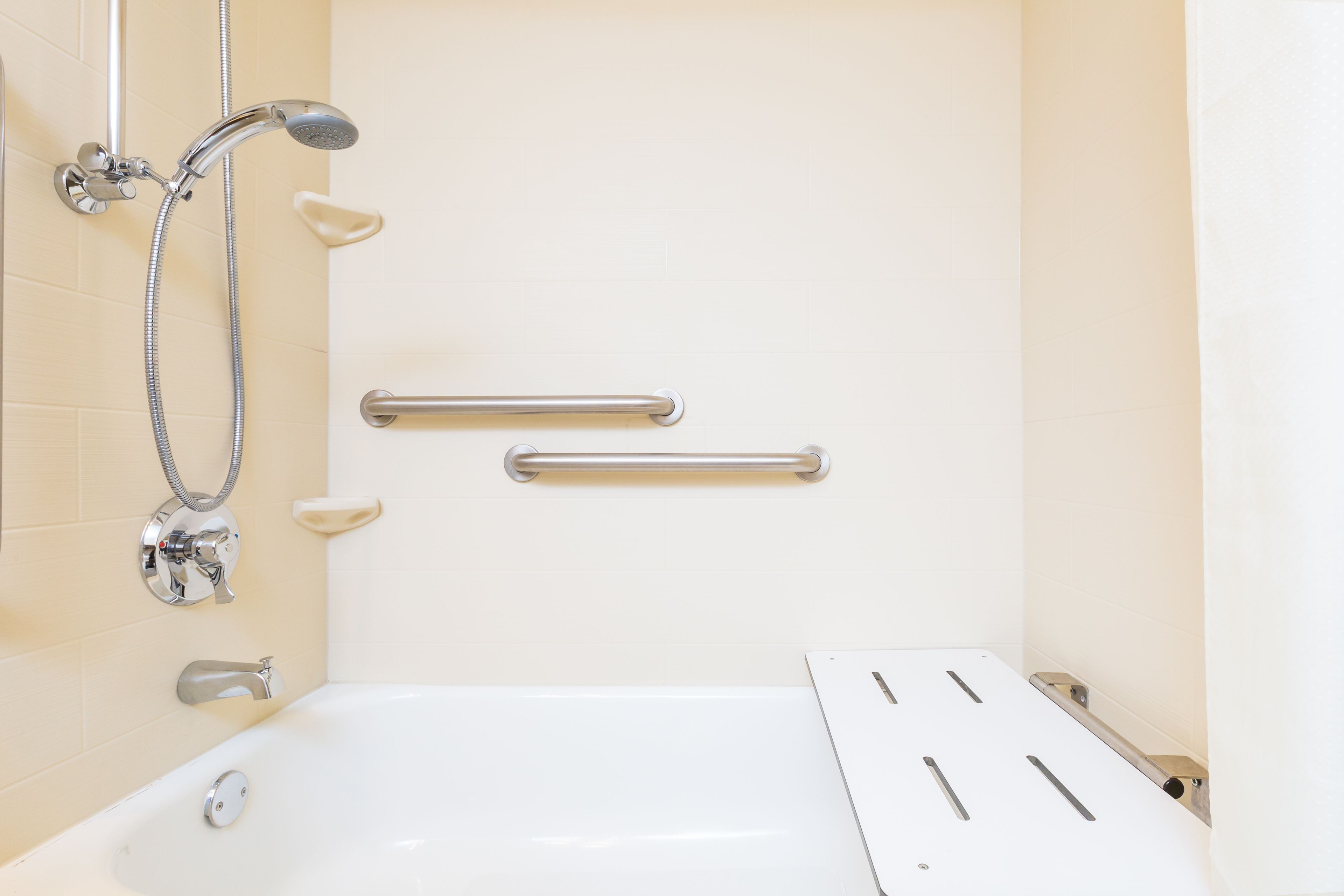 Un baño con una bañera blanca, un cabezal de ducha manual, un accesorio de ducha manual y dos barras de apoyo en la pared.
