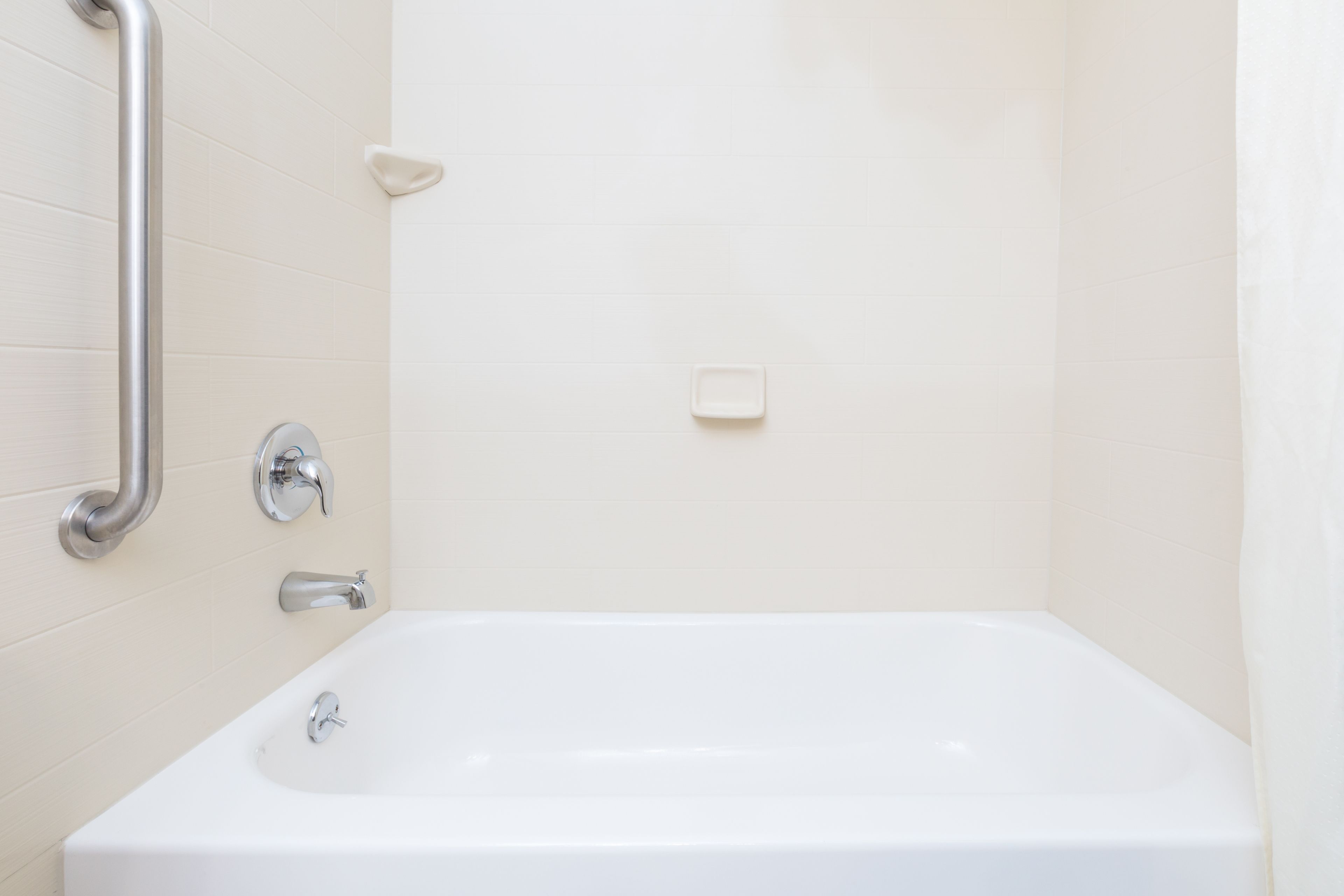 Una bañera blanca con una ducha de mano, un asidero y un jabonera en la pared.