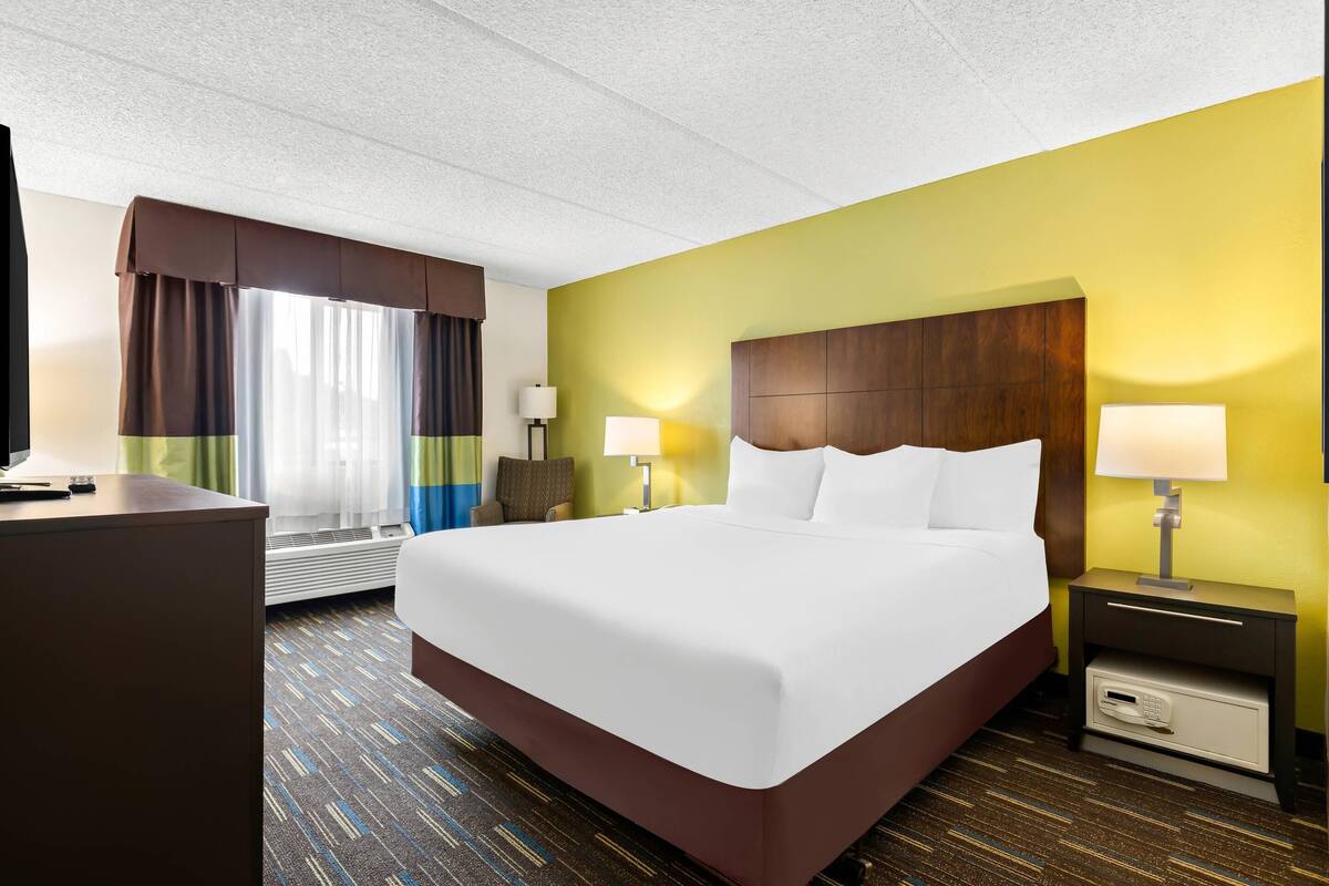 A hotel room with a large bed, two bedside tables with lamps, a desk, and a window with curtains.