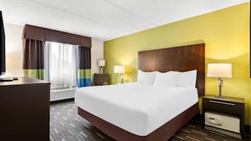 Une chambre d’hôtel avec un grand lit, deux tables de chevet avec des lampes, un bureau et une fenêtre avec des rideaux.