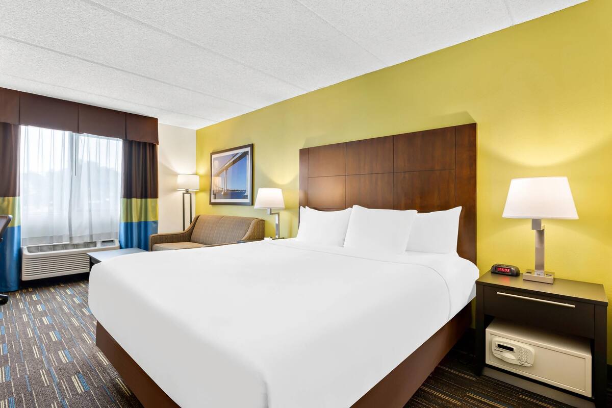 A hotel room with a large bed, two bedside tables with lamps, a chair, a desk, and a wall-mounted picture.
