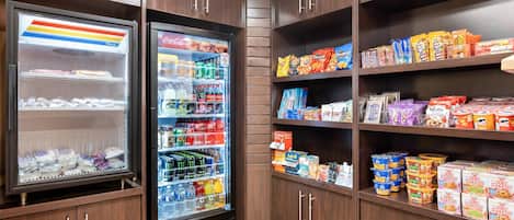 A snack and beverage refrigerator stocked with various drinks and snacks, surrounded by wooden cabinets with multiple shelves.
