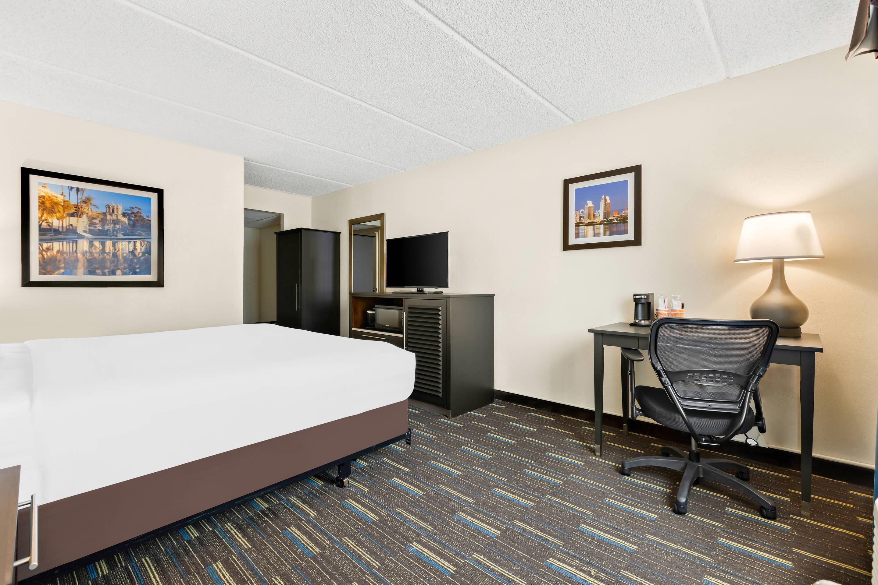 A hotel room with a bed, desk, chair, television, and two framed pictures on the walls.
