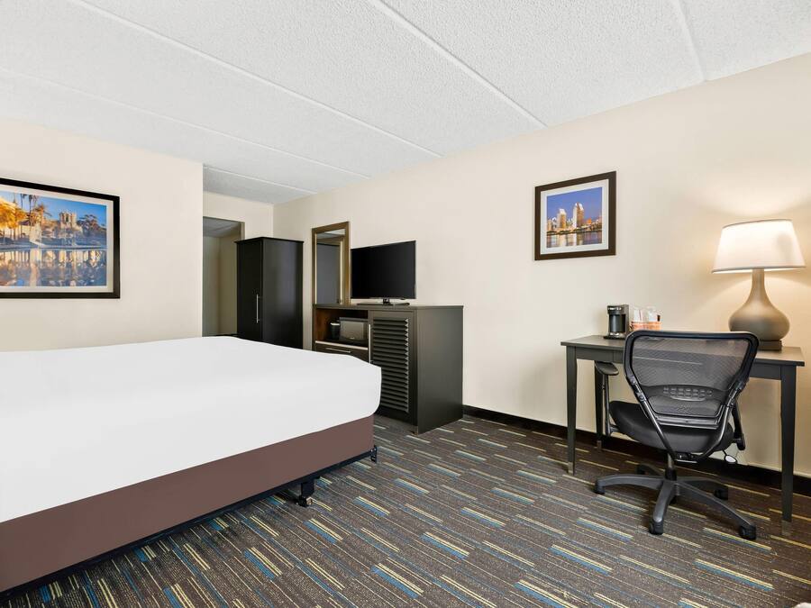 A hotel room with a bed, desk, chair, television, and two framed pictures on the walls.