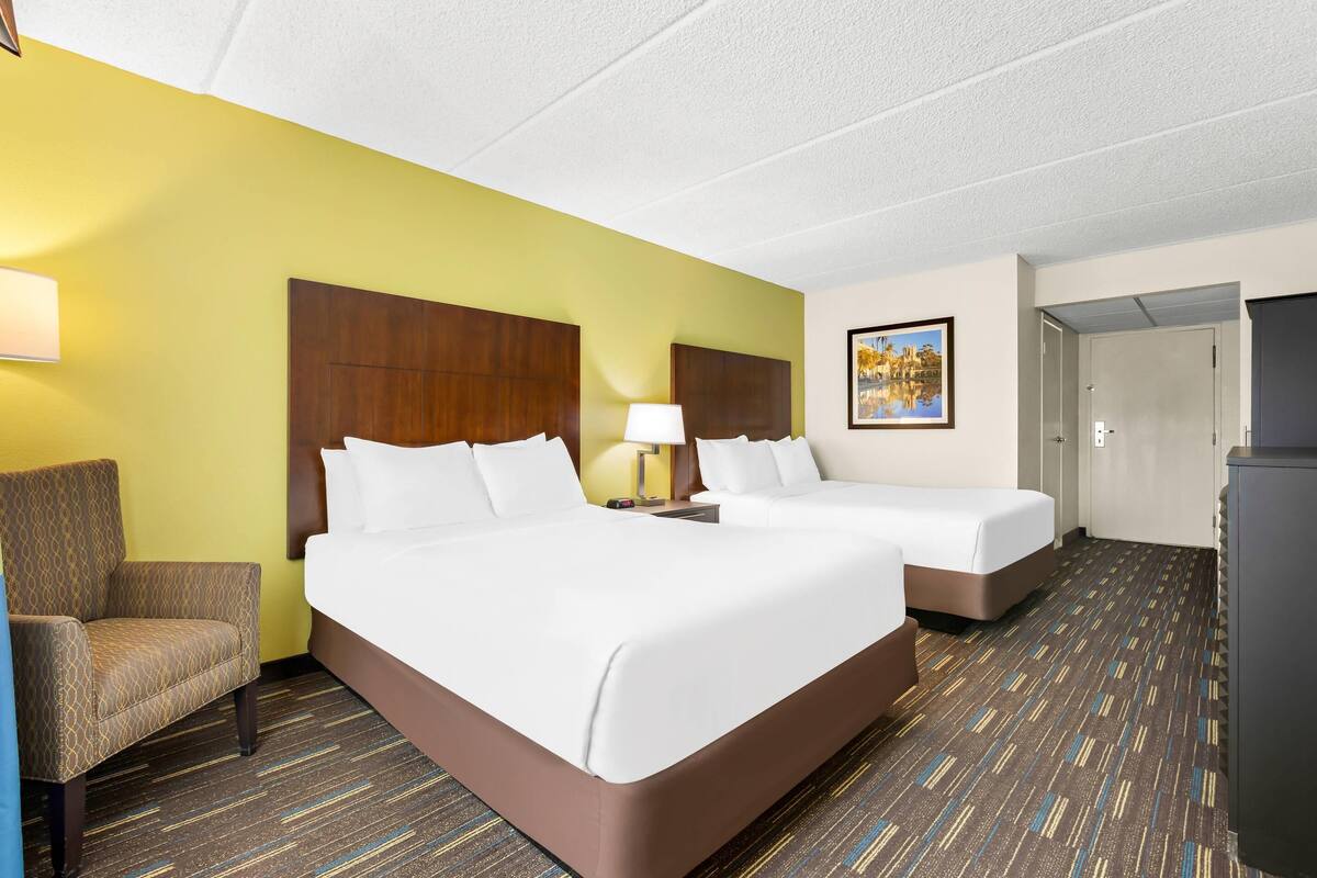 A hotel room with two beds, a chair, a desk, and a lamp.