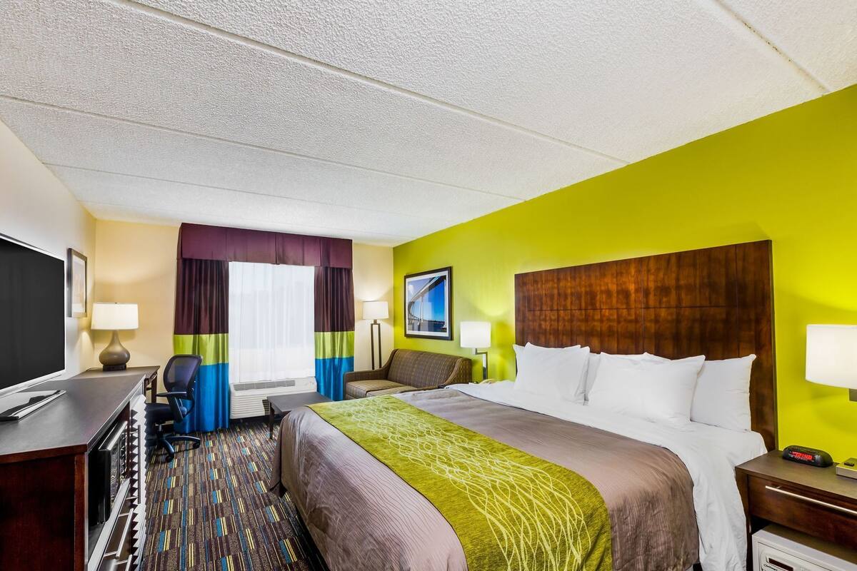 A hotel room with a bed, desk, chair, and a television.