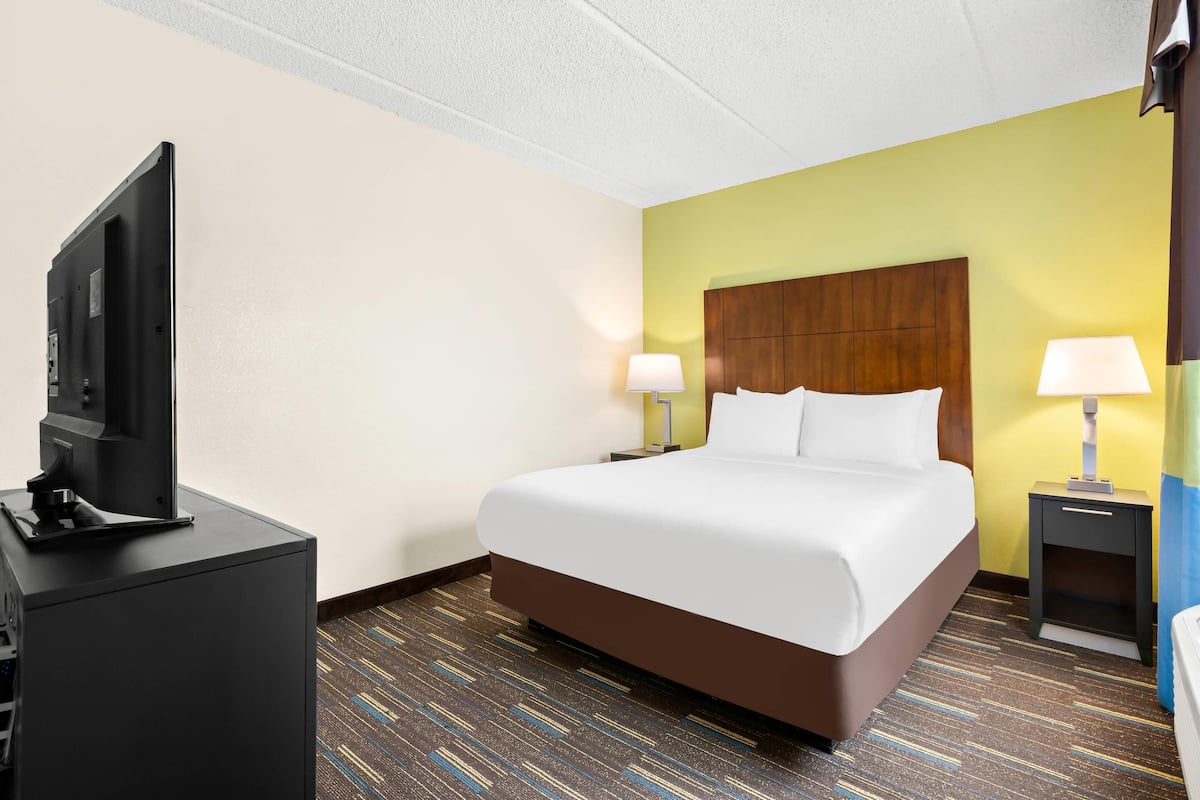 A hotel room with a bed, a TV on a stand, two bedside lamps, and a nightstand with a lamp.