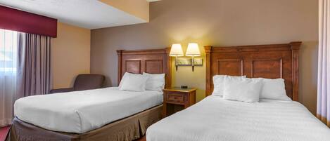 A hotel room with two beds, a chair, a nightstand with lamps, and a window with curtains.