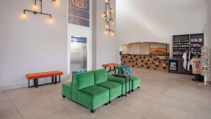 Een hal met een groene bank, oranje zitbanken, een receptiebalie en een kledingrek.