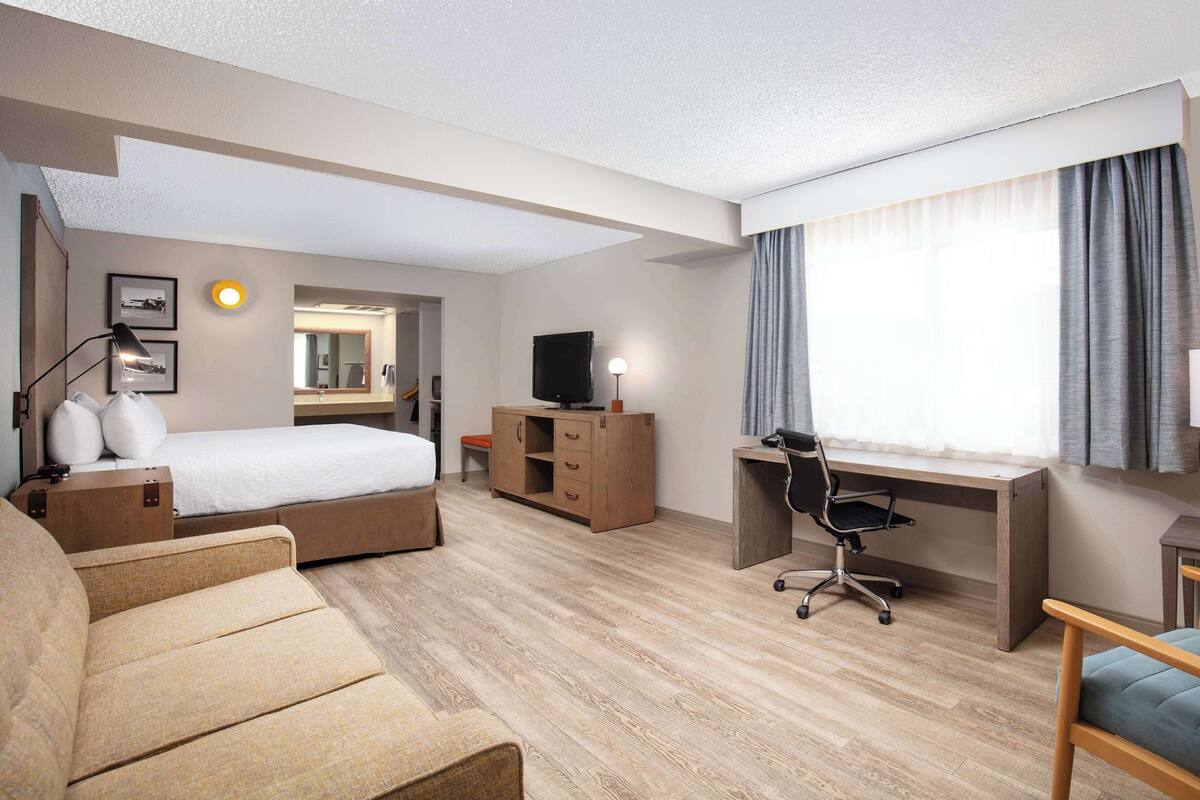 A hotel room with a bed, desk, chair, and a sofa.