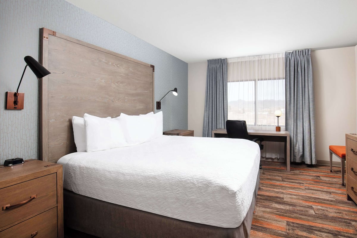 A hotel room with a large bed, a desk, a chair, a television, and a dresser.