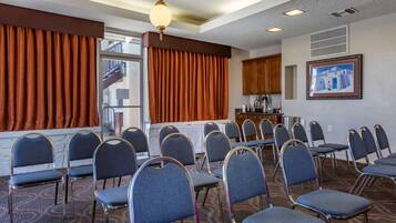 Une salle de conférence avec des rangées de chaises, une table et une vue sur un bâtiment à l’extérieur.