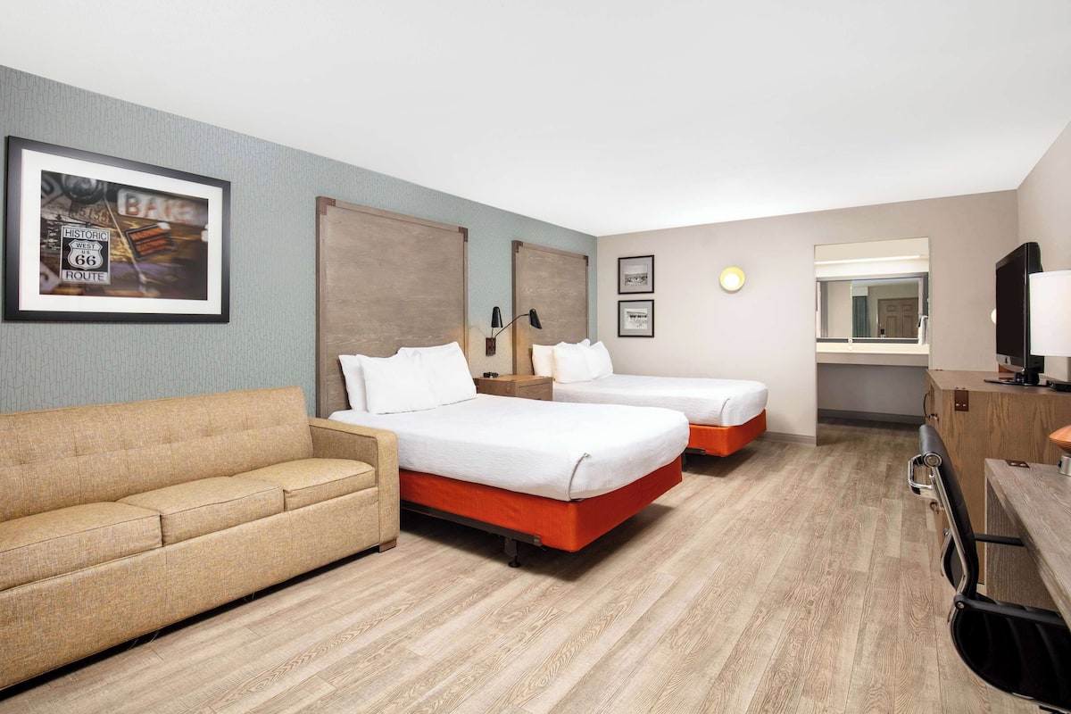 A hotel room with two beds, a sofa, a desk with a computer, and a mirror.
