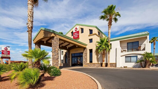 Een hotel met een Best Western PLUS bord, stenen zuilen, palmbomen en een heldere lucht.