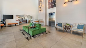 Een ruime lobby met een groene bank, houten stoelen, een flatscreen televisie en een trap naar een lift.