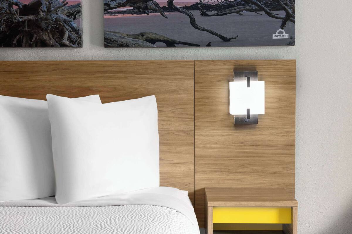 Una habitación de hotel con cabecera de madera, una mesita de noche con detalle amarillo y una obra de arte en la pared.