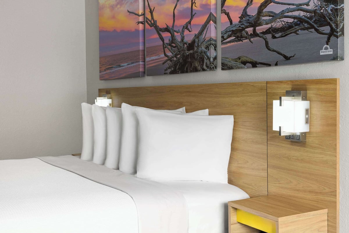 Una cama bien tendida con ropa de cama blanca, un cabecero de madera y una mesita de noche con un cajón amarillo.