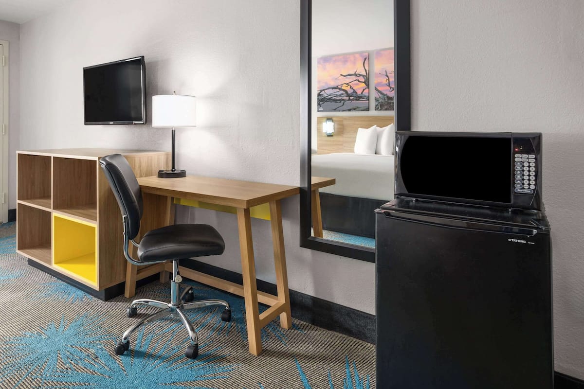 Habitación de hotel con escritorio, silla, televisor, microondas y cama con mesita de noche.
