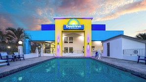 A Days Inn by Wyndham with a swimming pool, outdoor seating, and a sunset sky.